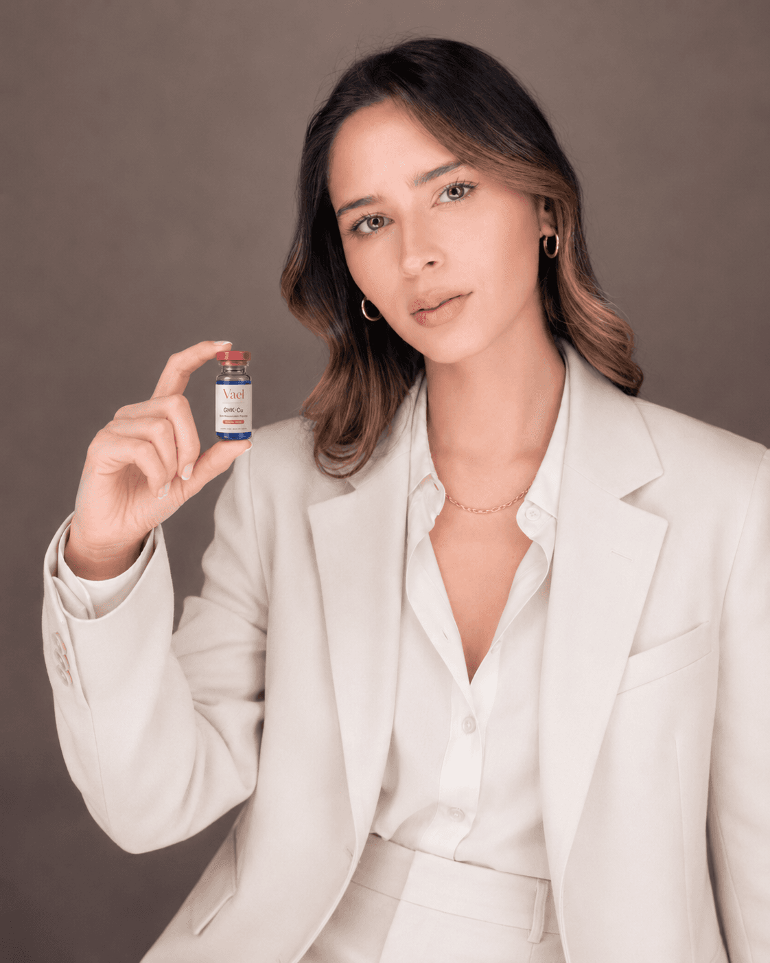 Woman in a cream suit holding a Vael GHK-Cu vial